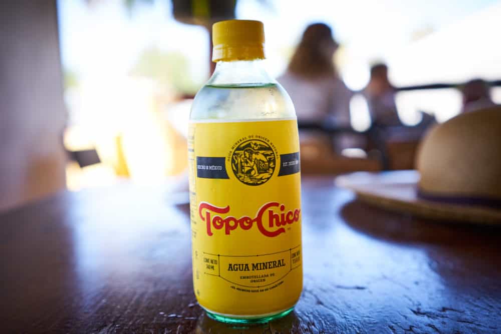 A bottle of Topo Chico water on a wooden table. 