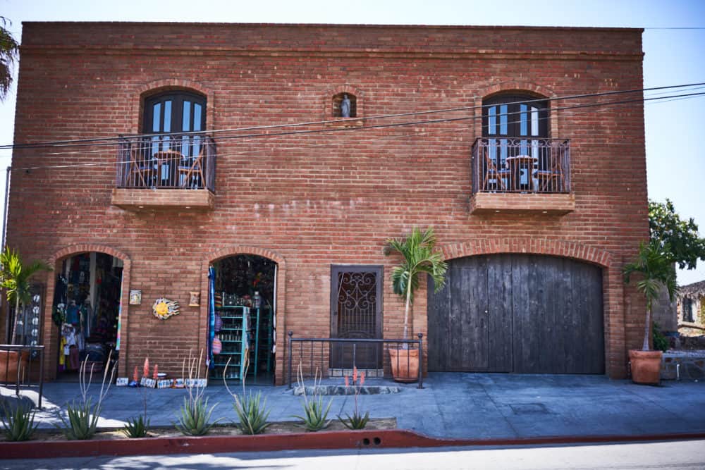 A two-story brick building with a storefront and a wooden garage door in Todos Santos, Mexico. 