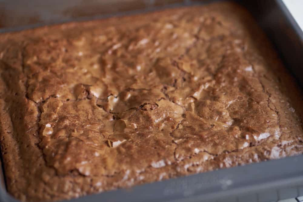 Baked brownies cooling in a square baking pan on a wire rack.