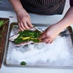 A woman's hands are shown preparing a salt baked whole fish, she stuffs a whole fish with lemon, lime and fresh herbs.