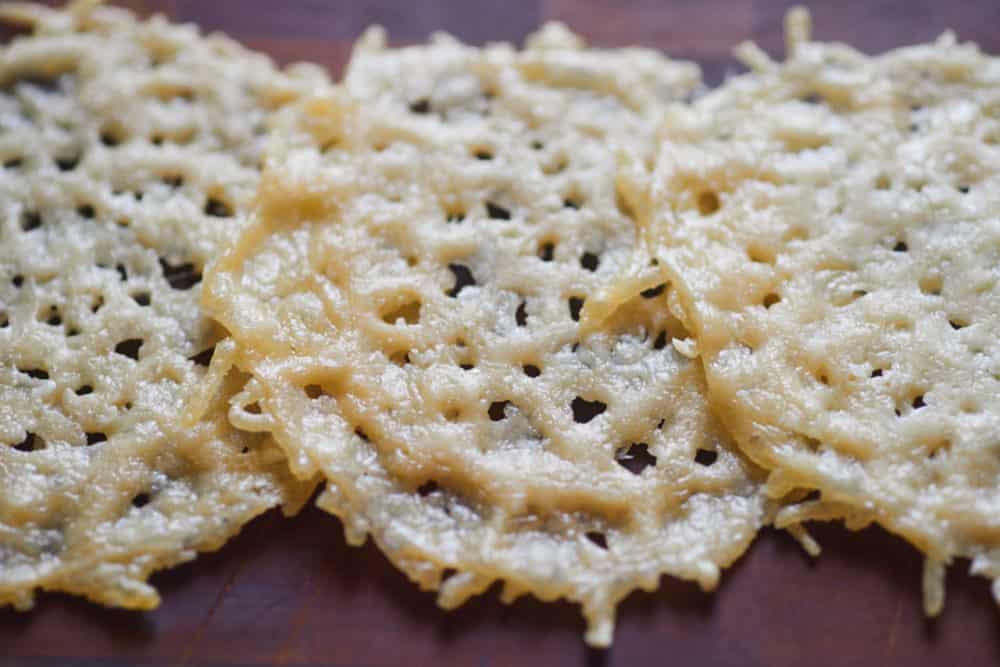 Cooked frico - parmesan crisps - on a wooden cutting board.