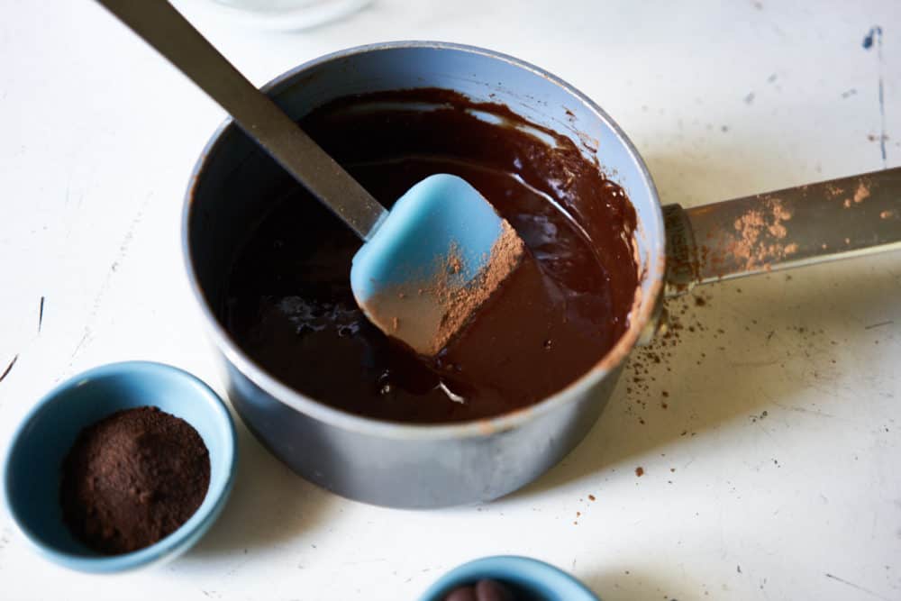 A small sauce pan with melted chocolate and a blue spatula. 