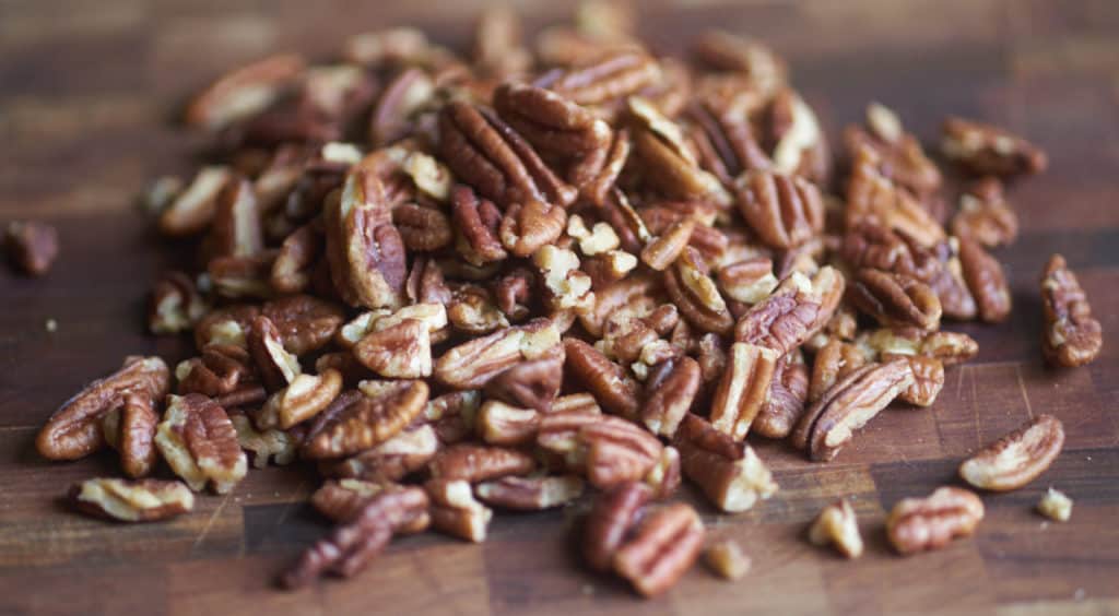Roughly chopped pecan halves on a wooden cutting board.