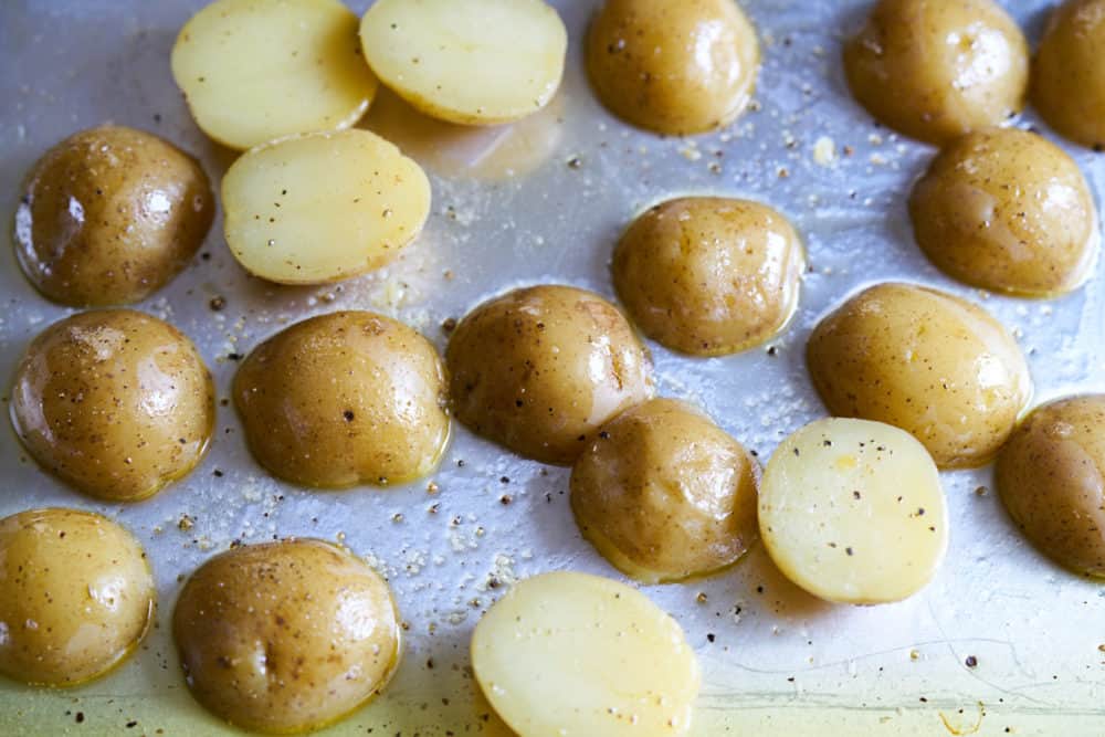 Yukon gold potatoes after being partially baked on a sheet tray coated with olive oil and seasoned with salt and pepper.