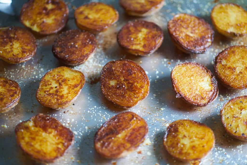 Crispy roasted potatoes seasoned with salt and pepper on a sheet tray with a silver spatula.