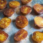 Crispy roasted potatoes seasoned with salt and pepper on a sheet tray with a silver spatula.
