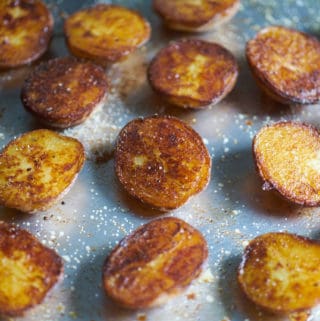 Crispy roasted potatoes seasoned with salt and pepper on a sheet tray with a silver spatula.