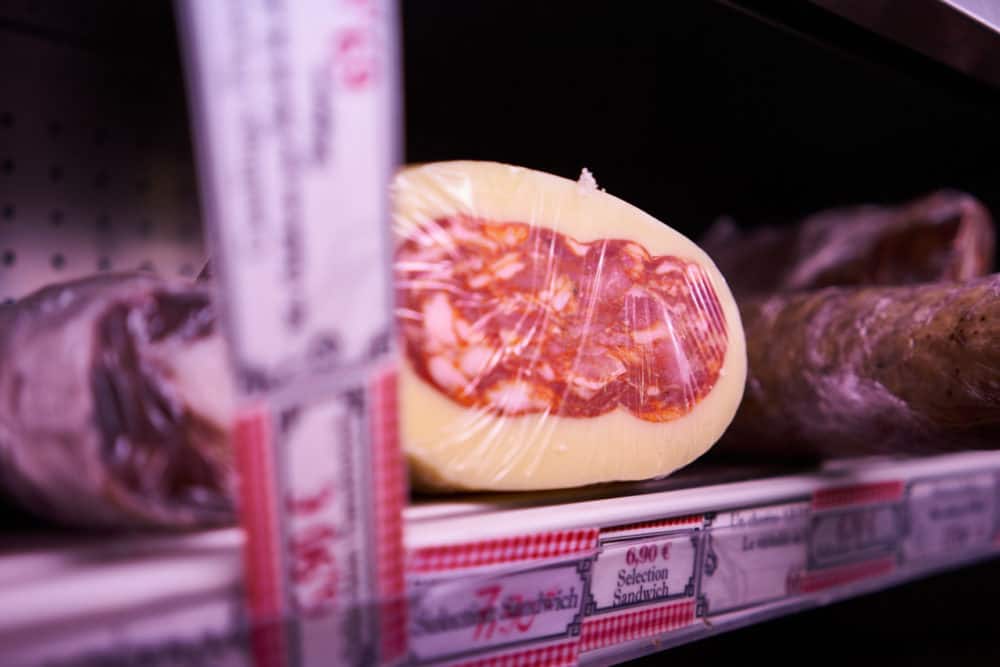 Caciospinata - a spicy soppresata wrapped in provolone cheese on a shelf in a refrigerated case at Caractère de Cochon, a charcuterie shop in the Marais neighborhood of Paris. 