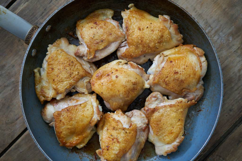 8 chicken thighs for Chicken Escabeche with crispy skin are nestled into a wide skillet.