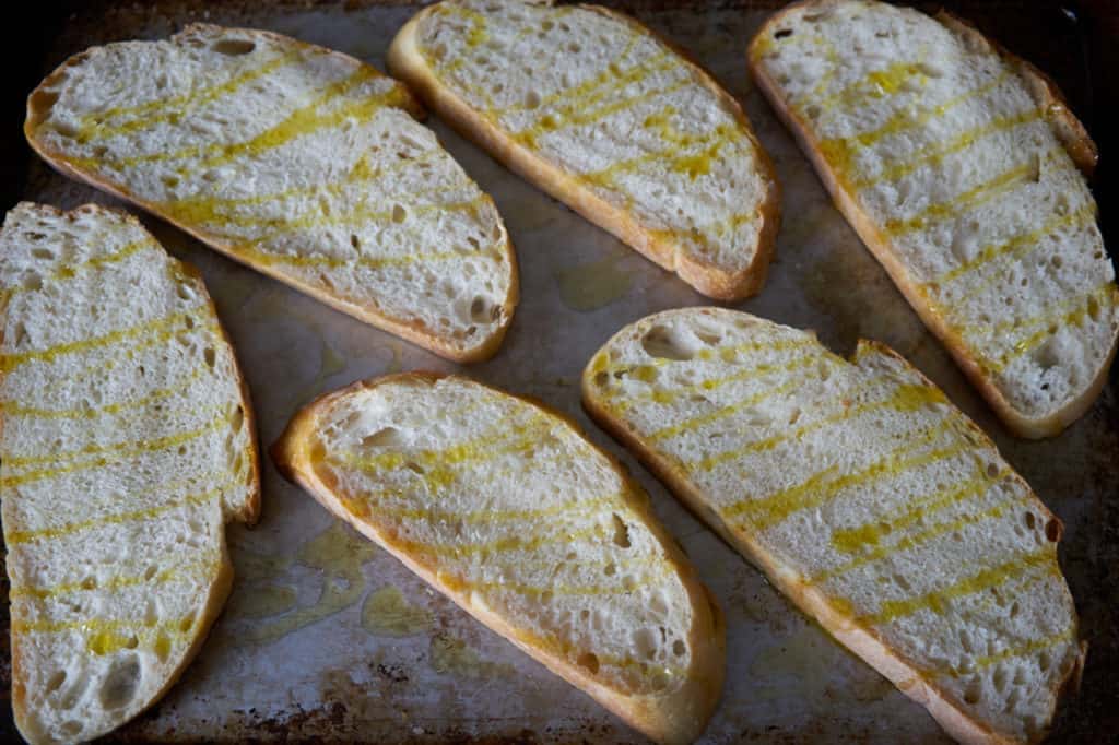 Slices of sourdough bread for tartines drizzled with olive oil on a baking sheet.