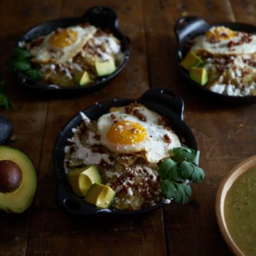 Portions of green chilaquiles topped with eggs in small cast iron dishes.
