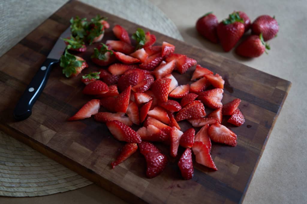 Sliced strawberries on a wooden cutting board with a small paring knife.