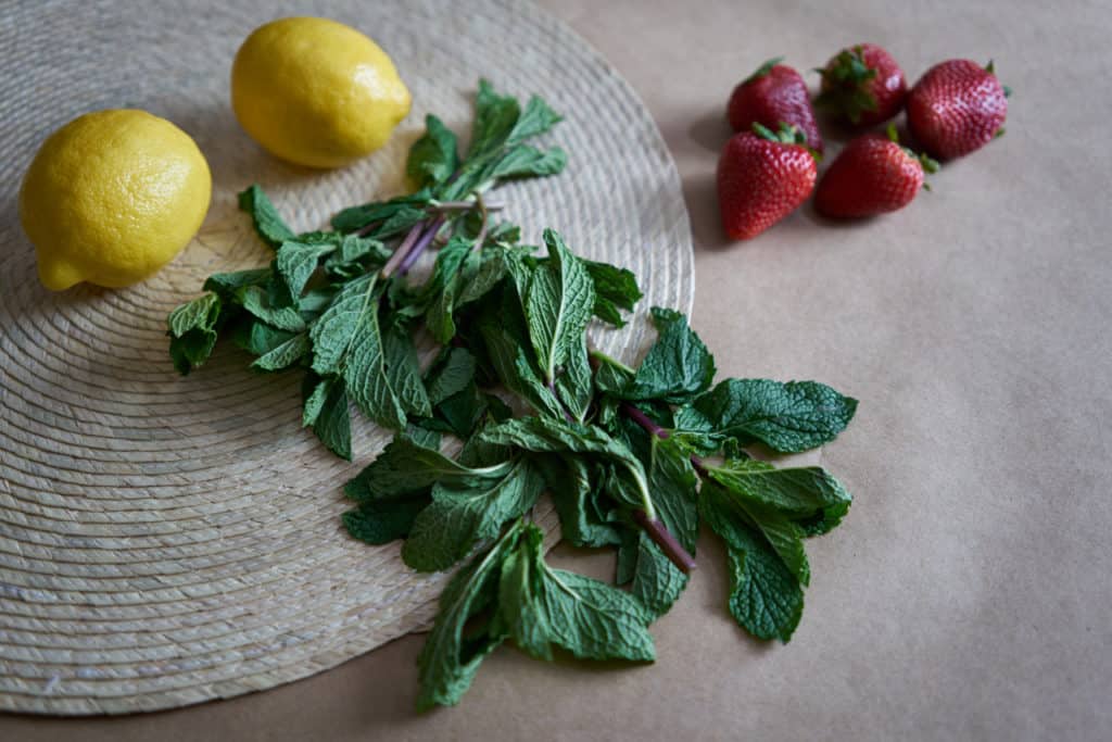 Fresh mint, lemons, and strawberries on a woven placemat.