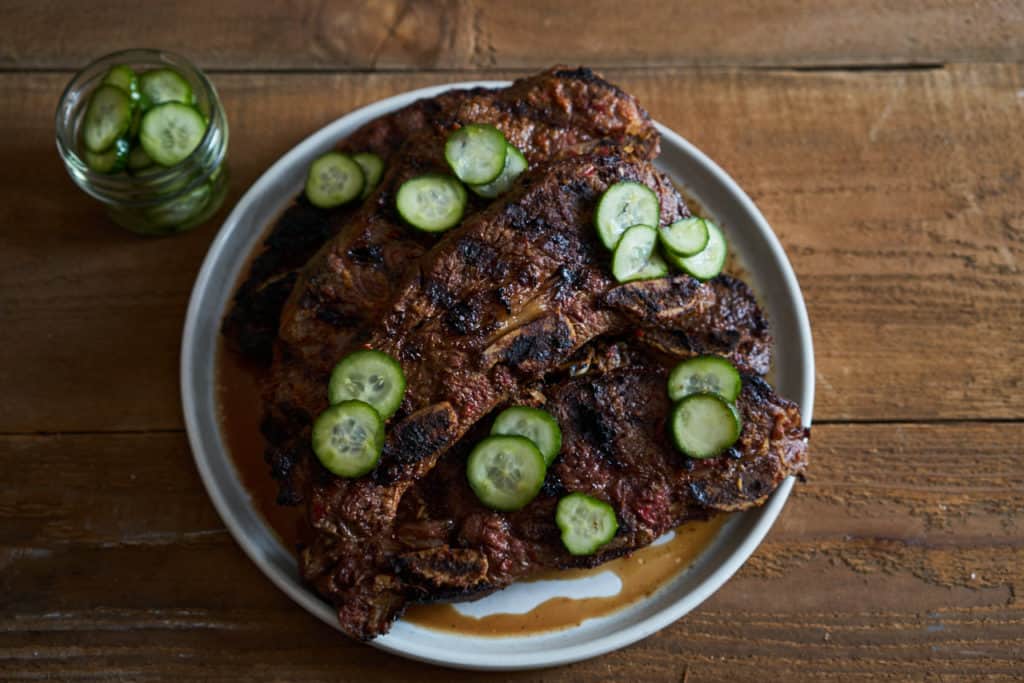 Grilled beef short ribs on a white plate topped with quick pickles.