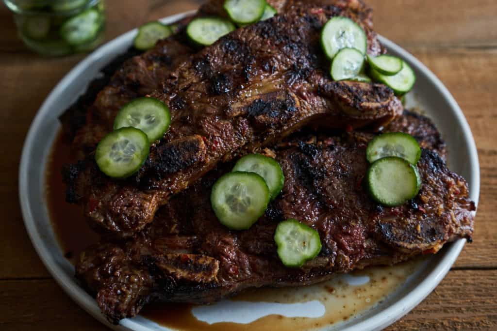 Grilled beef short ribs on a white plate topped with quick pickles.