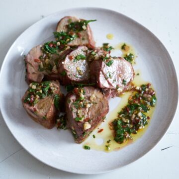 Slices of grilled pork tenderloin with chimichurri sauce on a white plate.