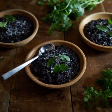 3 wooden bowls of Mexican black beans and fresh cilantro on a wooden table.
