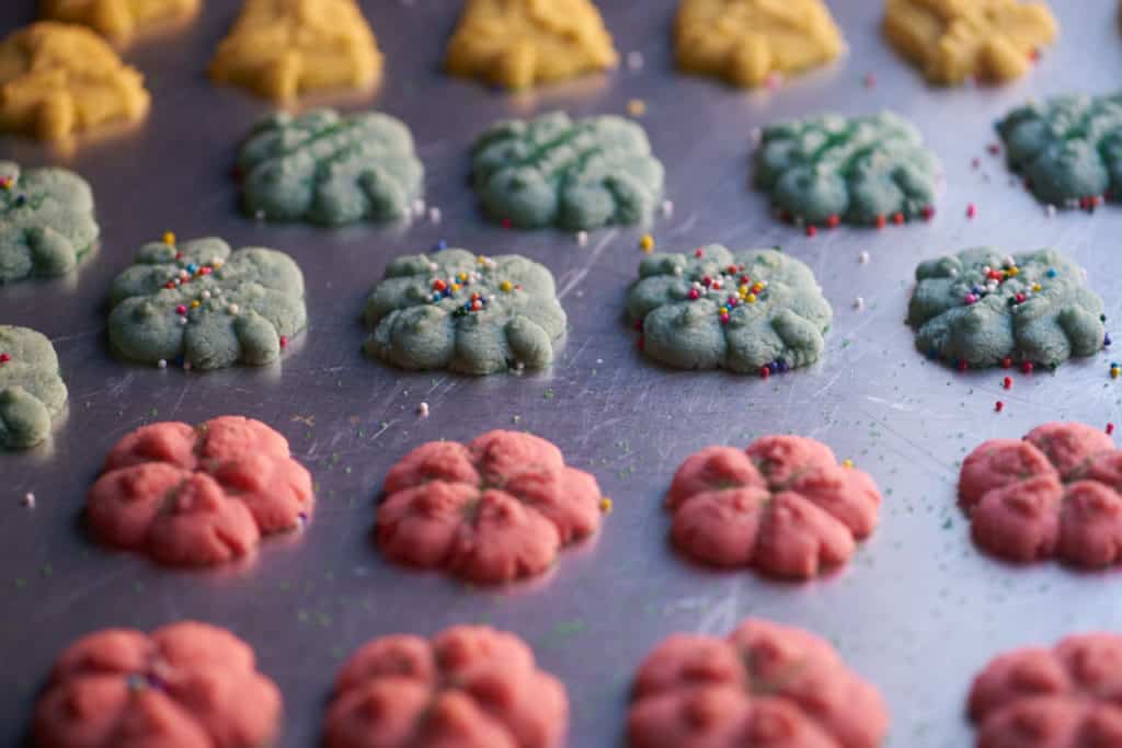 Red, blue, and green Spritz cookies of various shapes on a baking sheet. 