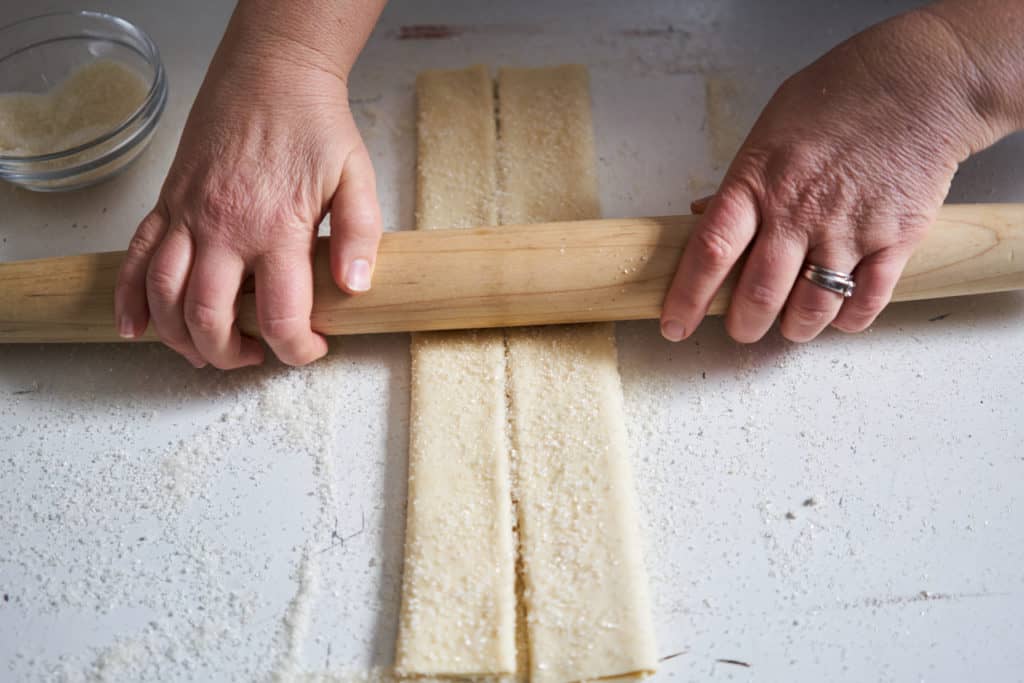 A woman's hands are shown with a wooden rolling pin, rolling out puff pastry. 