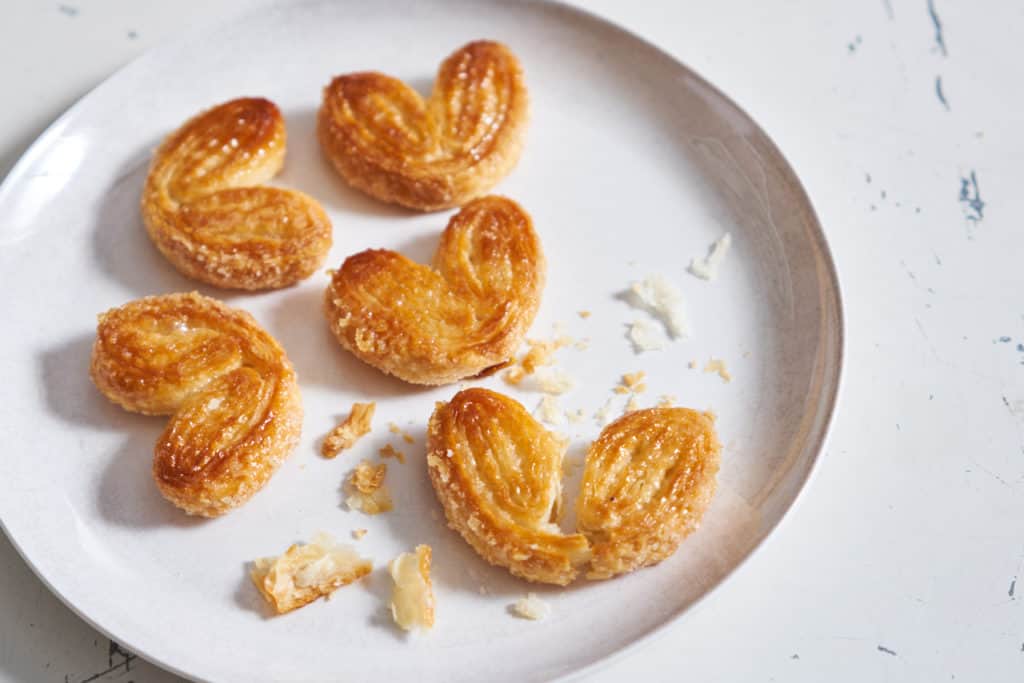 A white plate with palmiers, one is broken and crumbs are strewn over the plate.