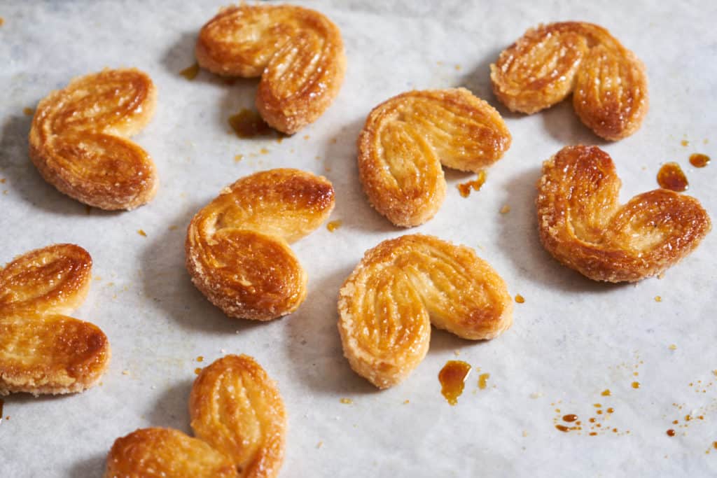 Sweet palmiers made of puff pastry on parchment paper with drops of caramelized sugar. 