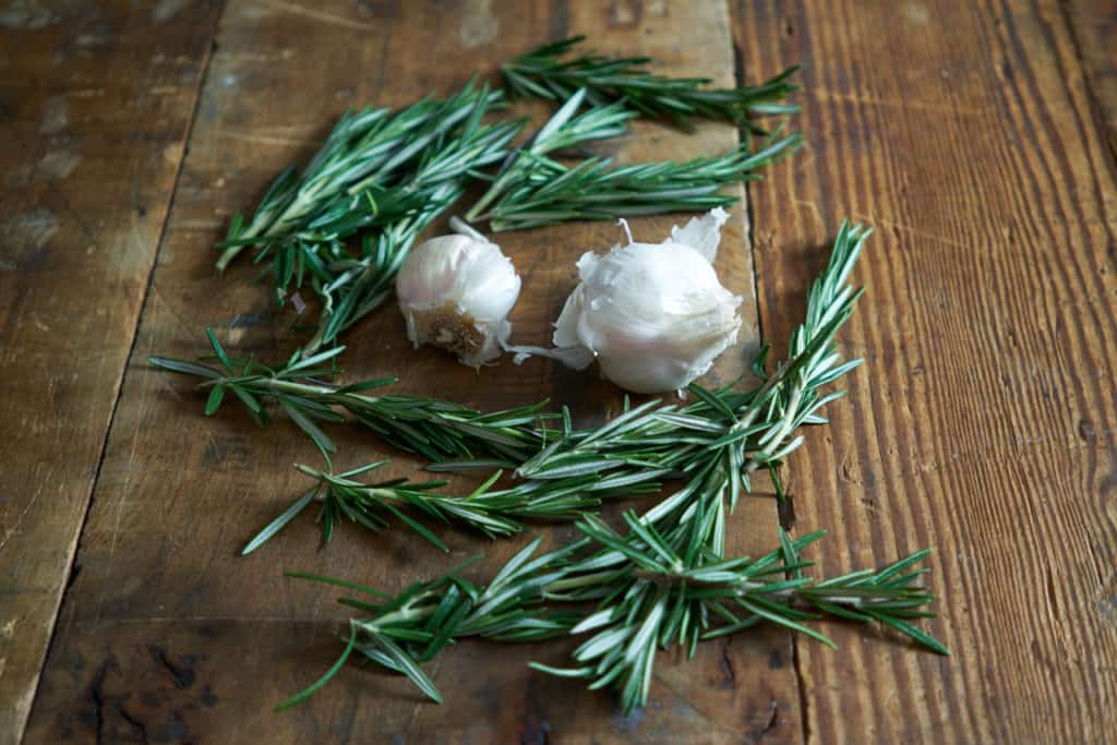 Fresh rosemary sprigs and two garlic cloves on a wooden surface.