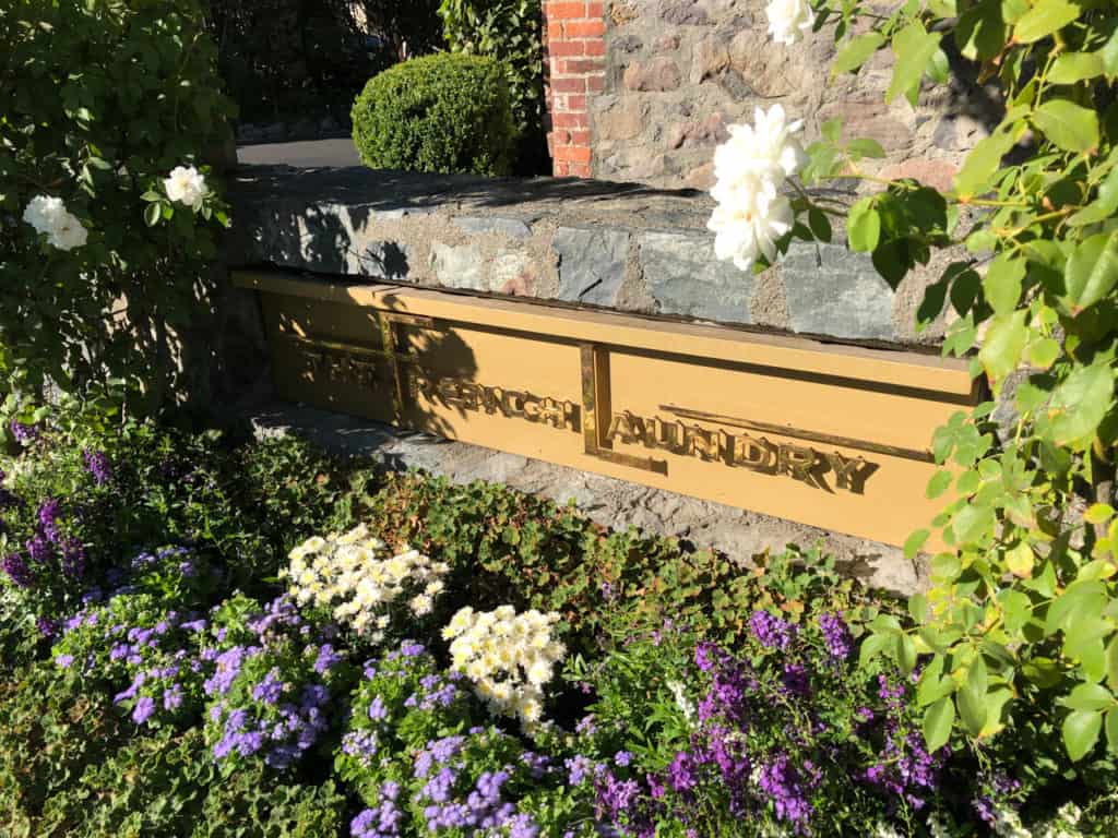 The French Laundry sign in front of the restaurant in bright sunlight.