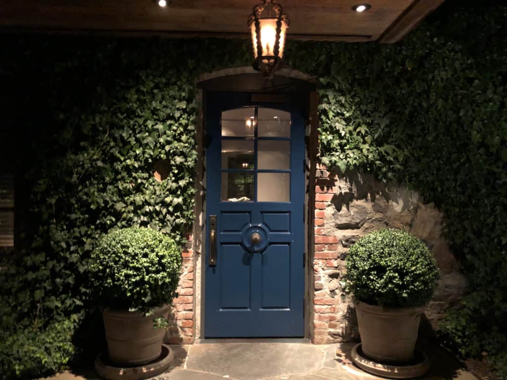 A blue door in a brick wall surrnounded by greenery. The entrance to The French Laundry.