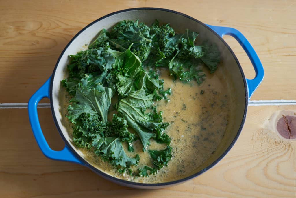 A blue enameled casserole dish with mustard sauce and chopped kale.