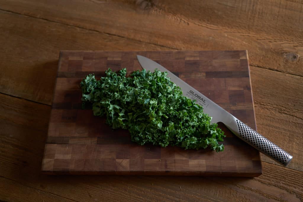 Chopped kale on a wooden cutting board with a chef's knife.