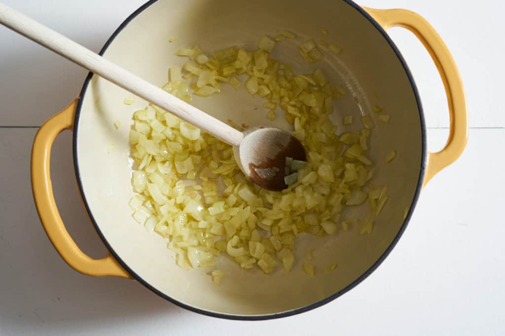 A yellow pot with sautéed onions and a wooden spoon.