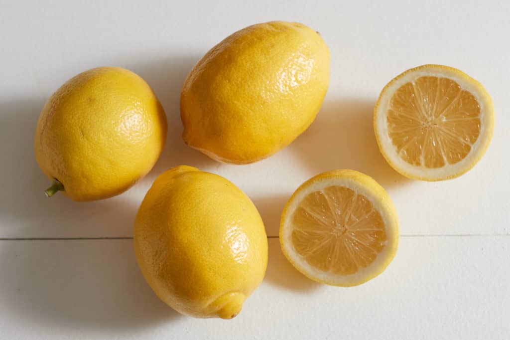 Three whole lemons and one lemon cut in half on a white surface.