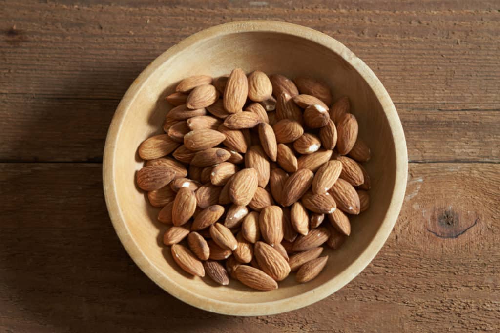 Whole almonds in a small wooden bowl.