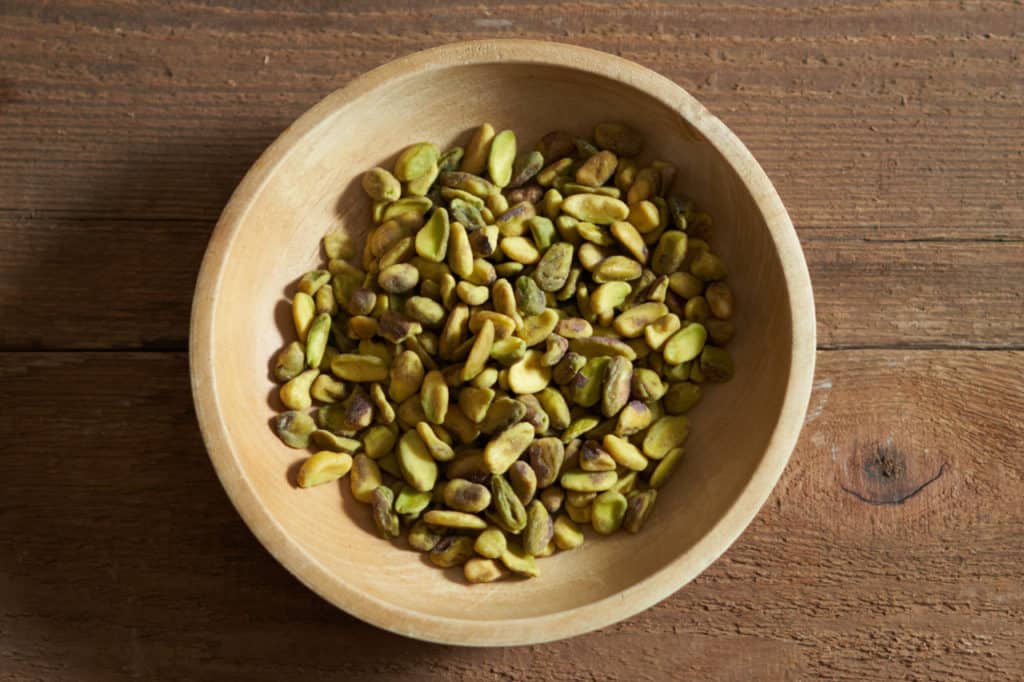 Whole pistachios in a small wooden bowl.