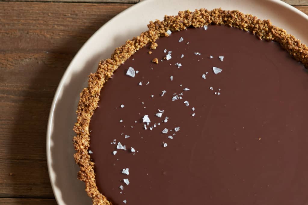 Gluten free chocolate tart topped with sea salt flakes on a pink plate.