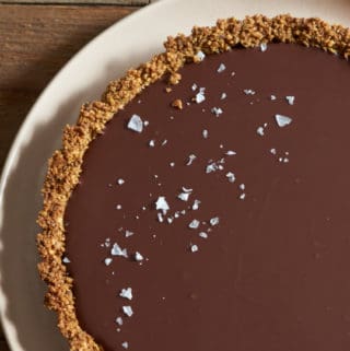 Gluten free chocolate tart topped with sea salt flakes on a pink plate.