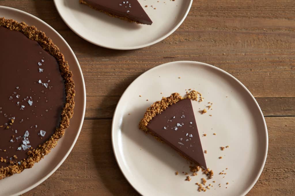 Slices gluten free chocolate tart topped with sea salt flakes on pink plates.