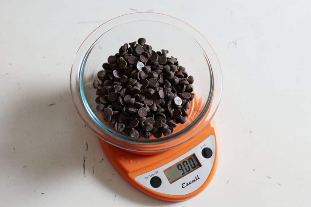 An orange kitchen scale with a bowl of chocolate chips on it.