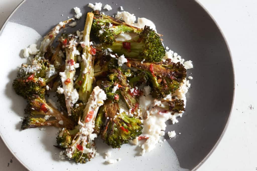 Charred broccoli with Calabrian chili paste on a grey and white plate.