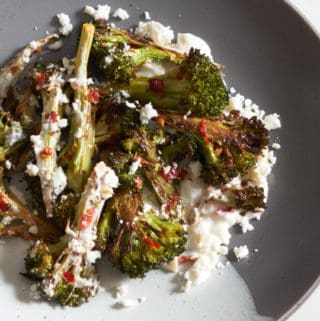 Charred broccoli with Calabrian chili paste on a grey and white plate.