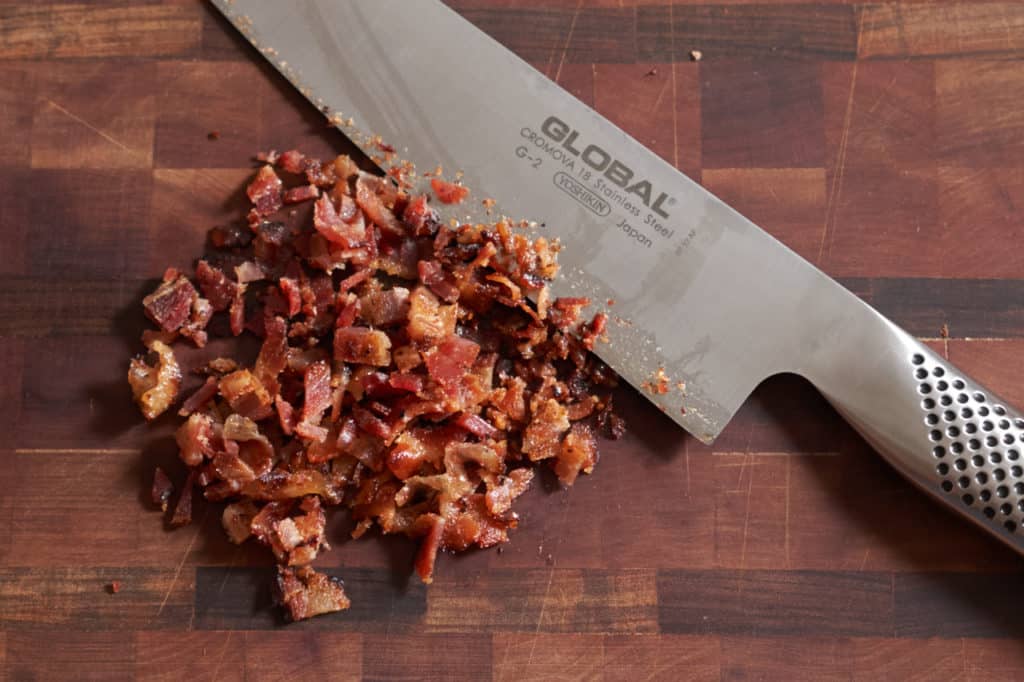 Chopped bacon and a chef's knife on a cutting board.