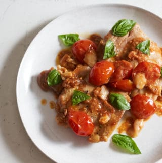 Chicken thighs with cherry tomatoes and fresh basil on a white plate.