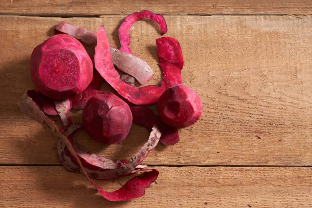 Peeled beets and beet peelings on a wooden surface.