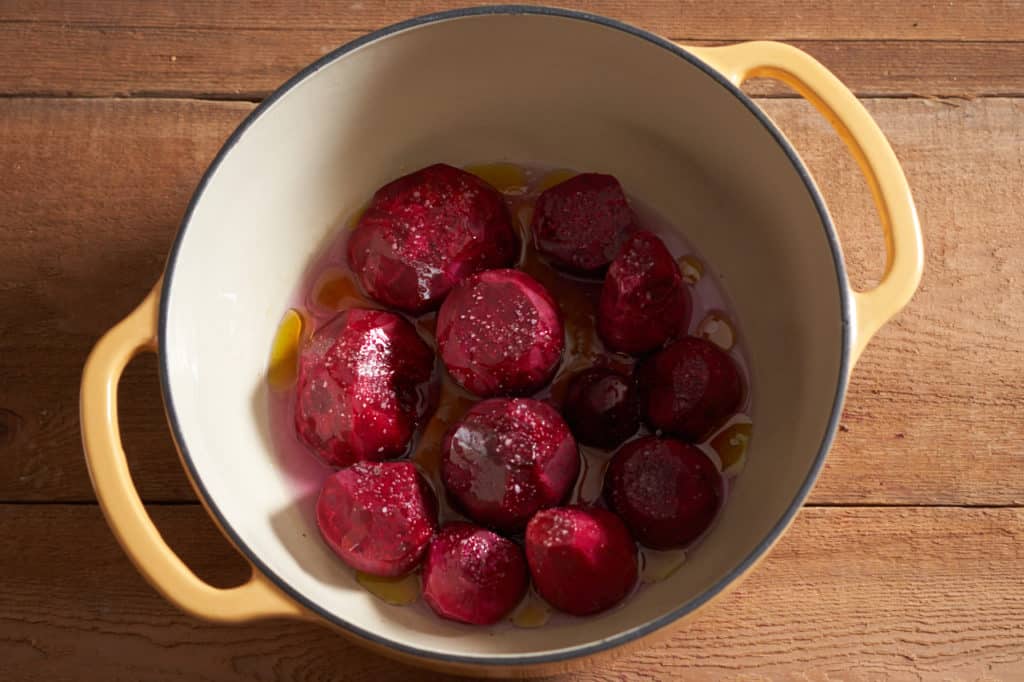Peeled beets in a Dutch oven seasoned with olive oil and salt, ready for roasting.