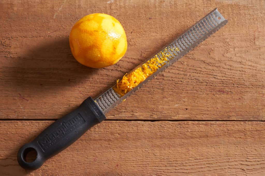 A fresh orange next to a microplane grater with orange zest.