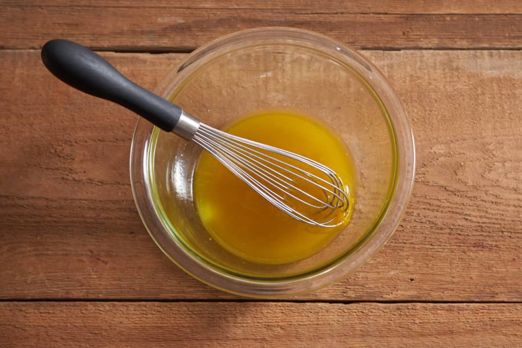 A whisk sits in a glass bowl of orange vinaigrette.