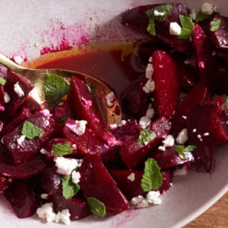 A gold spoon sits in a pink bowl full of oven-roasted beets with goat cheese, orange vinaigrette, and mint.