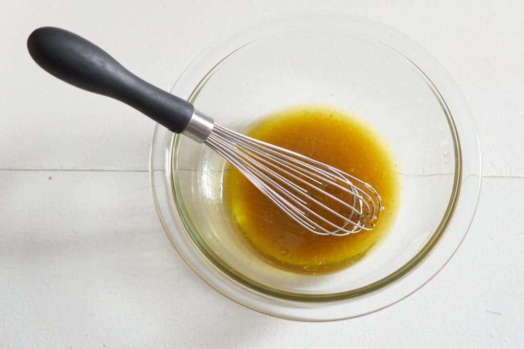 A whisk sits in a glass bowl of sherry vinegar sauce