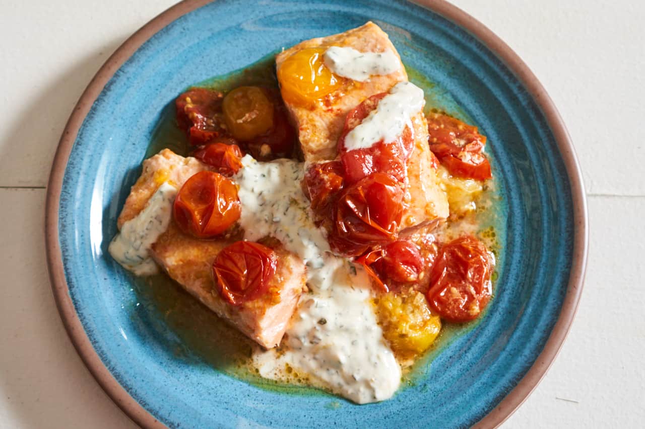 Oven baked salmon with roasted tomatoes and basil yogurt sauce on a blue plate.