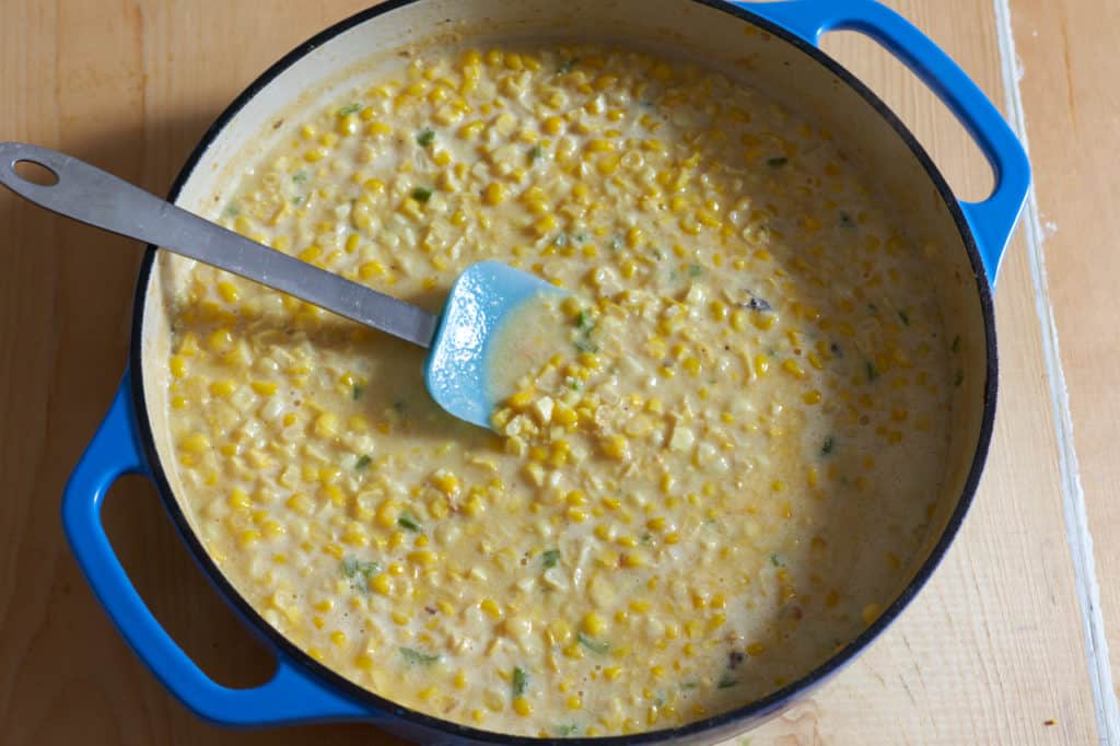 A blue casserole pan with corn kernels and serrano chiles that have been simmered in coconut milk.